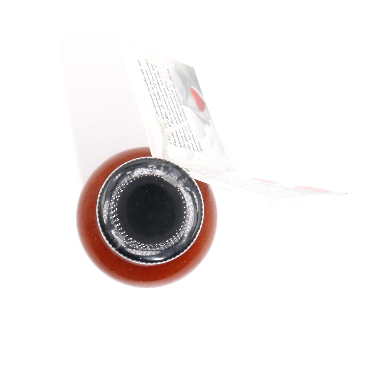 A close-up top-down view of a small round reddish-brown bottle or container with a black circular opening and a white paper label partially visible behind it, on a white background.