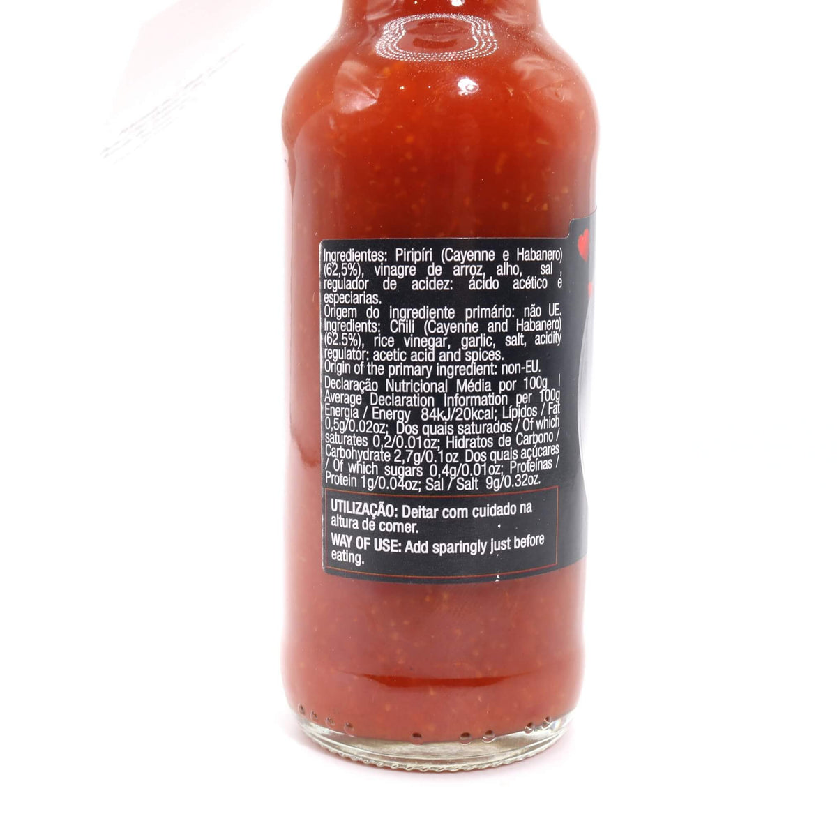 A close-up of the back of a glass hot sauce bottle filled with red sauce, showing a black label with white text on a white background.