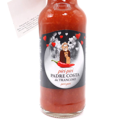 A glass bottle of Padre Costa de Trancoso piri-piri hot sauce with a black and white label featuring a cartoon character and red hearts, filled with red sauce, on a white background.