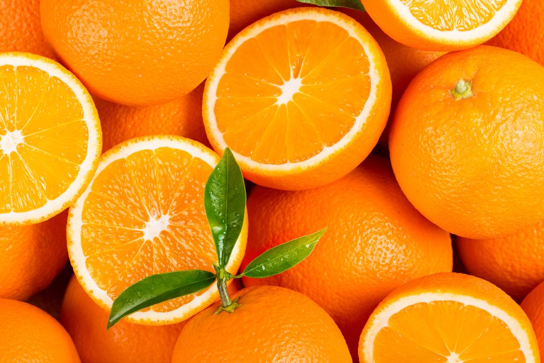 Oranges and orange halves with a green leaf on a pile of oranges.