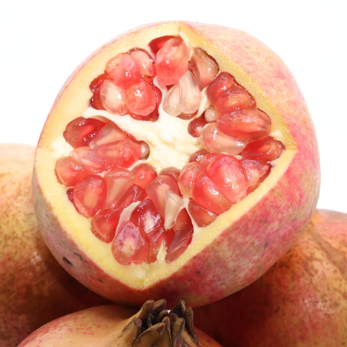 pomegranate with top cut off so that you can see the seeds, sitting on whole pomegranates with a white background.