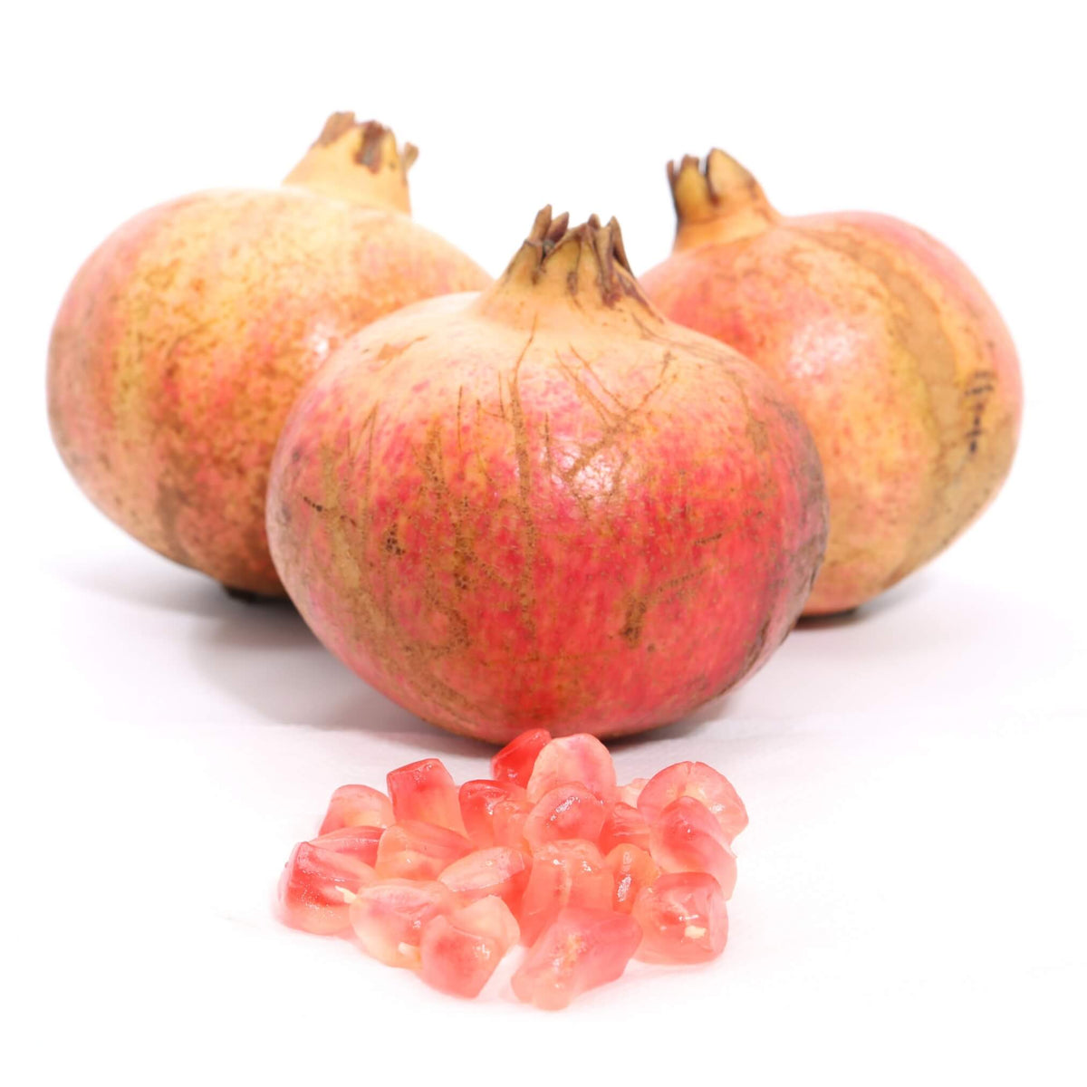 Three whole pomegranates with a small pile of pink-red arils in front, photographed on a clean white background.