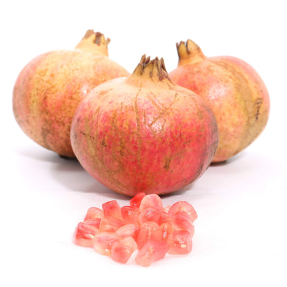 Three whole pomegranates with a small pile of pink-red arils in front, photographed on a clean white background.