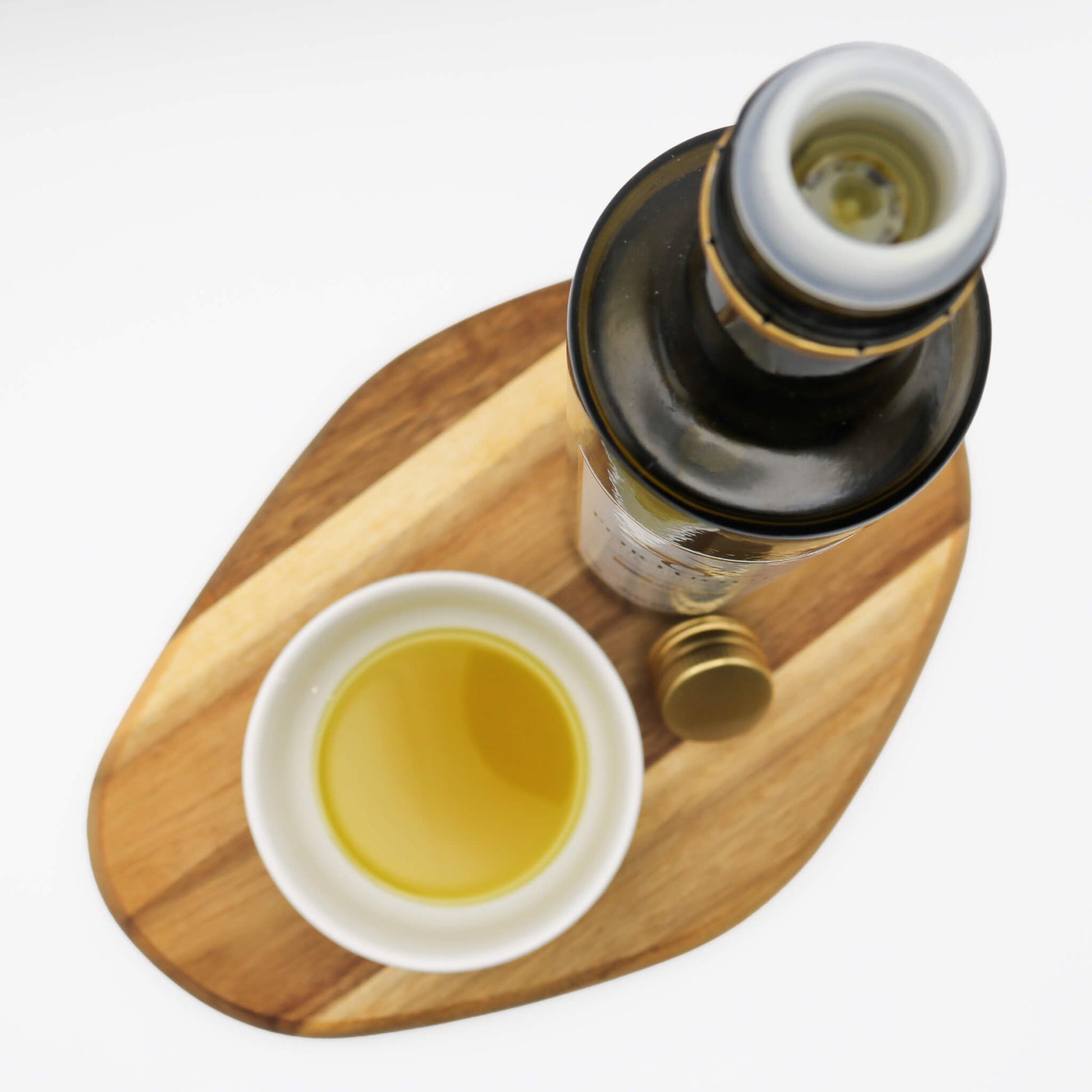 Bottle and small bowl of oil on a wooden board with a white background
